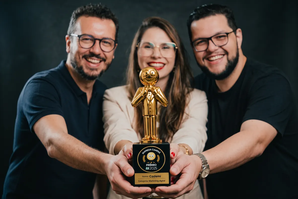 Matheus, Carol e Renan, da Cademí, segurando o troféu de empresa campeã do Prêmio Reclame AQUI 2025 na categoria Marketing Digital